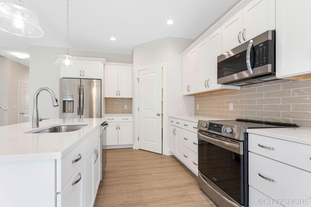 kitchen with pendant lighting, a center island with sink, sink, light wood-type flooring, and appliances with stainless steel finishes