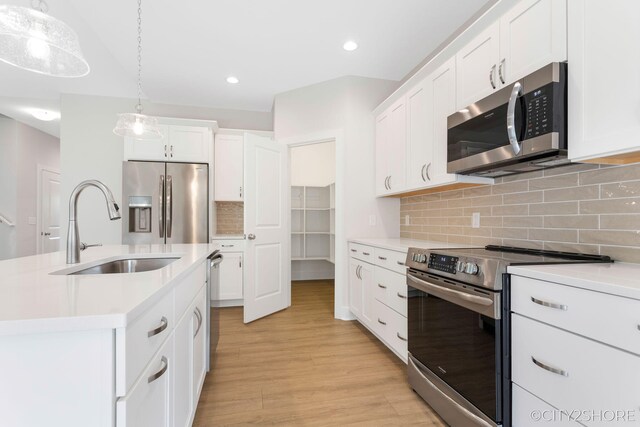 kitchen featuring appliances with stainless steel finishes, sink, decorative light fixtures, a center island with sink, and light hardwood / wood-style floors