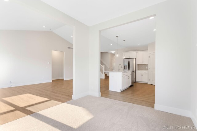 unfurnished living room featuring light wood-type flooring, sink, and vaulted ceiling