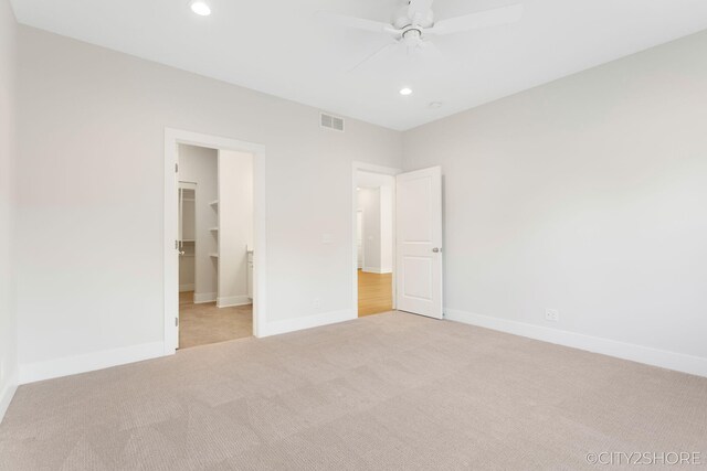 unfurnished bedroom with a walk in closet, light colored carpet, a closet, and ceiling fan