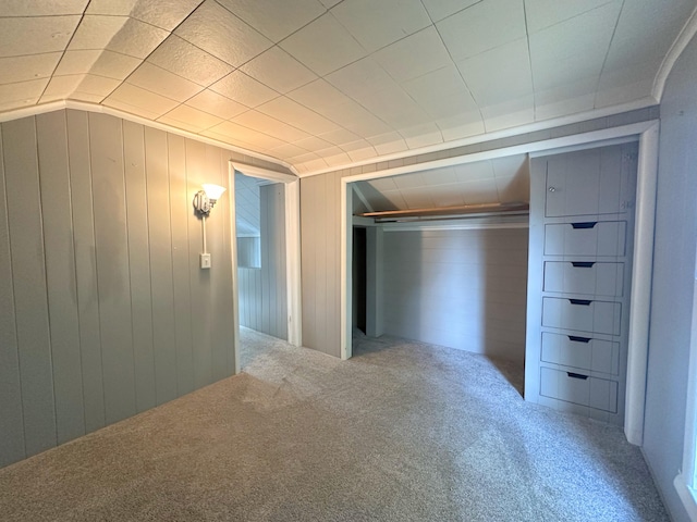 unfurnished bedroom with carpet, a closet, wooden walls, and vaulted ceiling