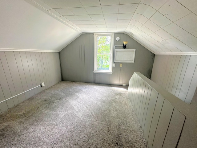 bonus room with wood walls, light carpet, and vaulted ceiling