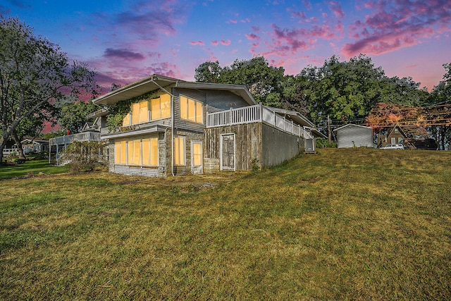 back house at dusk featuring a balcony and a yard