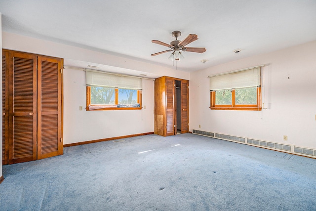 unfurnished bedroom featuring a baseboard heating unit, ceiling fan, light carpet, and multiple closets