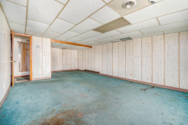 basement with a paneled ceiling, wood walls, and carpet floors