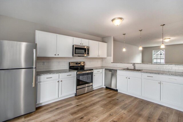 kitchen with stainless steel appliances, sink, white cabinets, and decorative light fixtures