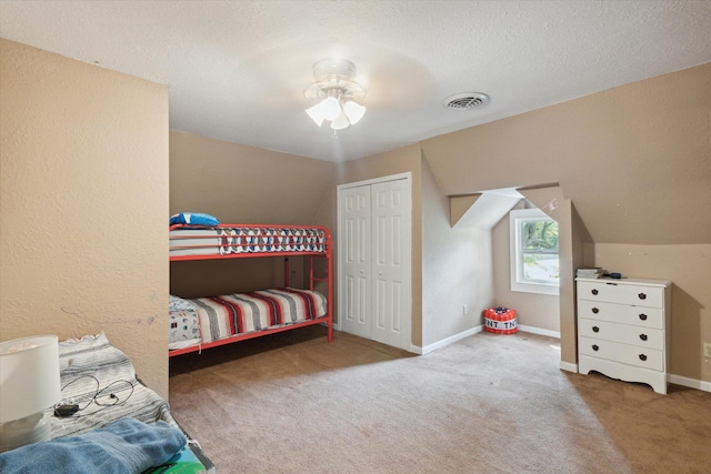 bedroom with a textured ceiling, a closet, carpet floors, lofted ceiling, and ceiling fan