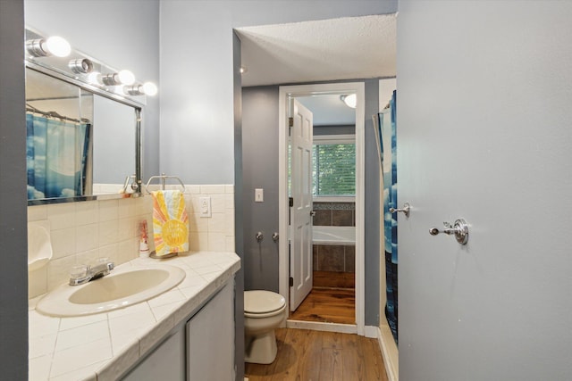 full bathroom featuring a textured ceiling, vanity, wood-type flooring, tasteful backsplash, and toilet