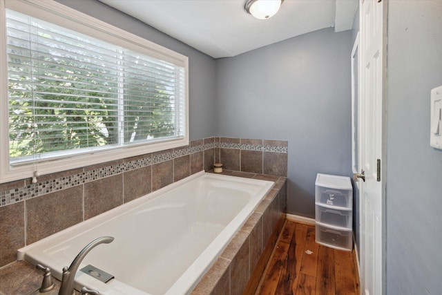 bathroom featuring a wealth of natural light, hardwood / wood-style floors, heating unit, and tiled bath