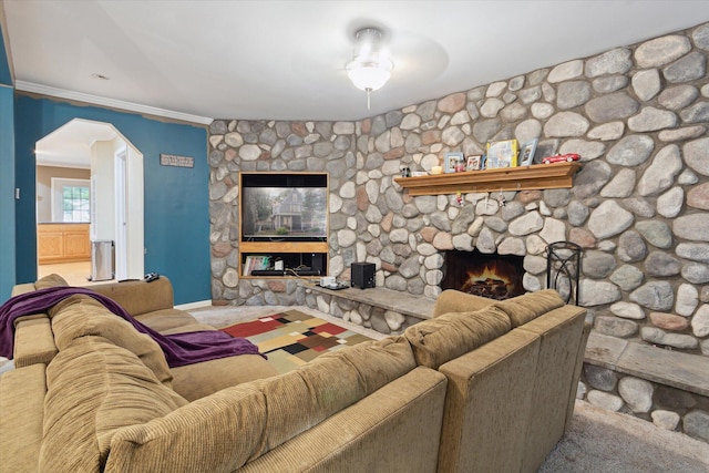 living room featuring crown molding, ceiling fan, a stone fireplace, and carpet floors