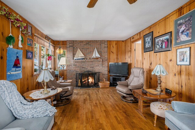 living room with a brick fireplace, hardwood / wood-style flooring, wooden walls, and ceiling fan