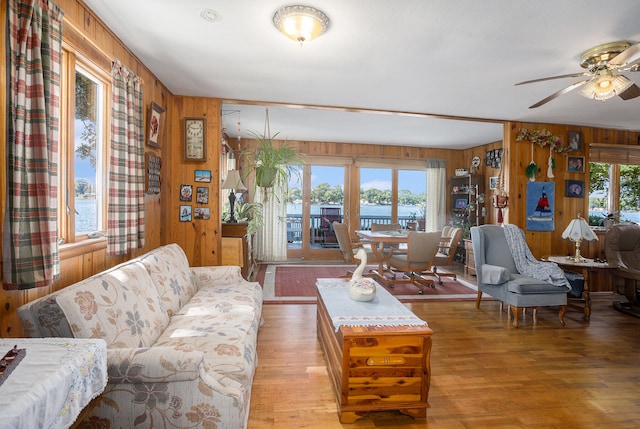 living room featuring wood-type flooring, wooden walls, and ceiling fan