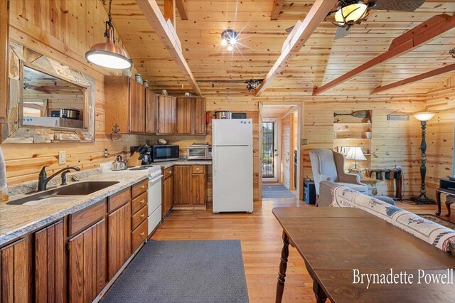 kitchen featuring white appliances, pendant lighting, light hardwood / wood-style floors, sink, and wooden walls