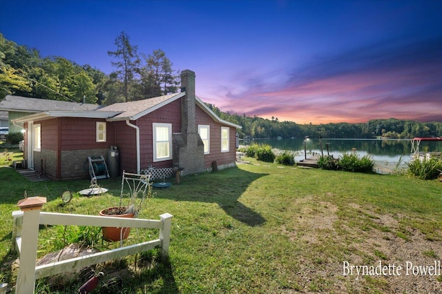 property exterior at dusk with a yard and a water view