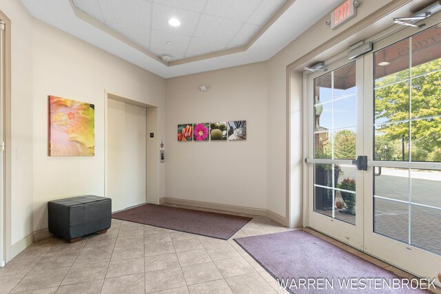 doorway with french doors, elevator, a tray ceiling, and light tile patterned flooring