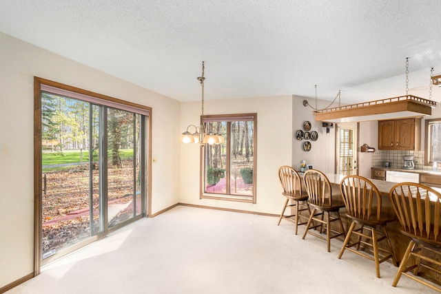 dining area with light colored carpet, a textured ceiling, a wealth of natural light, and a chandelier