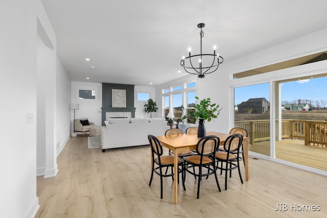 dining area with a fireplace, plenty of natural light, a chandelier, and light wood-type flooring