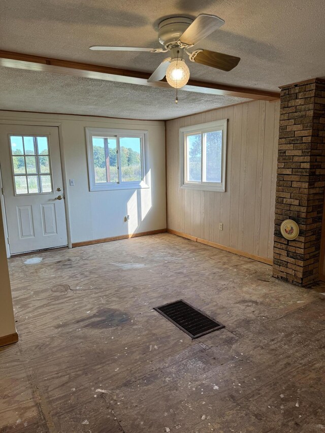 interior space with a textured ceiling, plenty of natural light, ceiling fan, and wooden walls