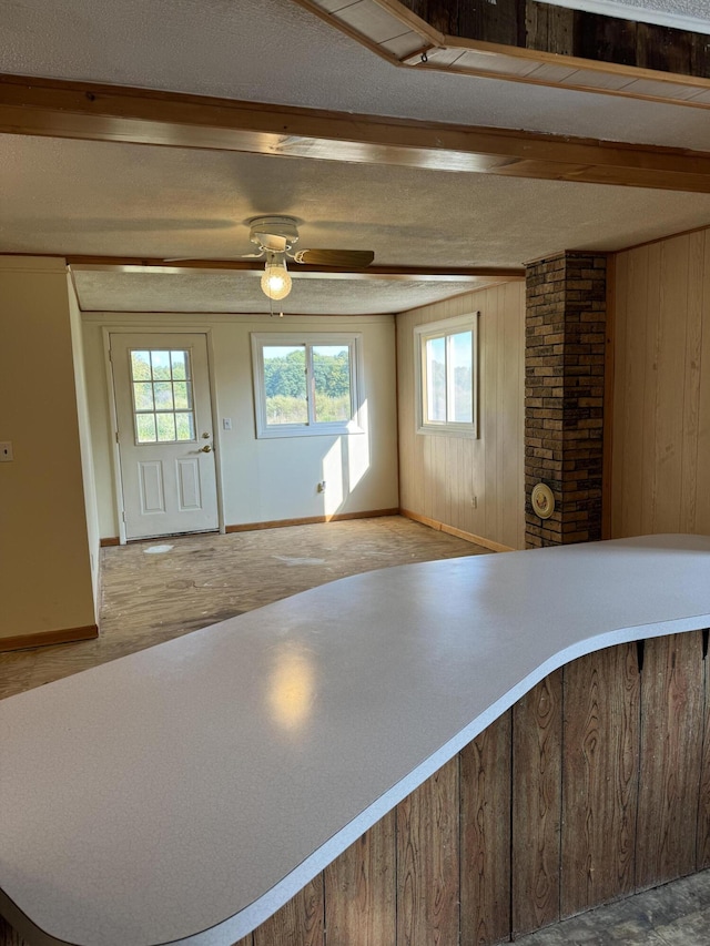 kitchen featuring beamed ceiling, a textured ceiling, ceiling fan, and wood walls