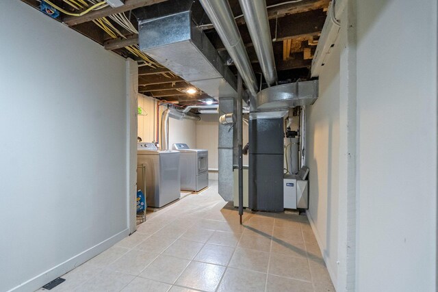 basement featuring light tile patterned floors, heating unit, and washing machine and dryer