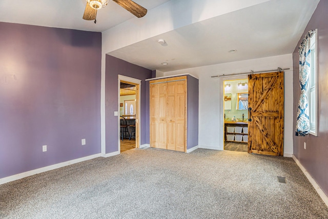 unfurnished bedroom featuring a barn door, carpet floors, ceiling fan, and a closet