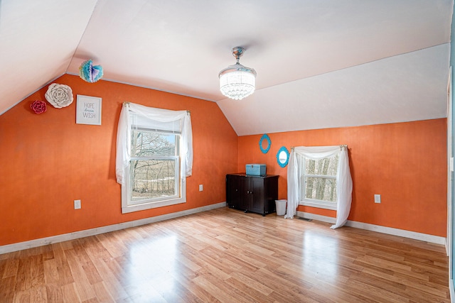 additional living space featuring a healthy amount of sunlight, lofted ceiling, and light hardwood / wood-style flooring