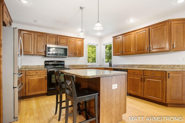 kitchen with light wood-type flooring, decorative light fixtures, stainless steel appliances, a kitchen breakfast bar, and a center island