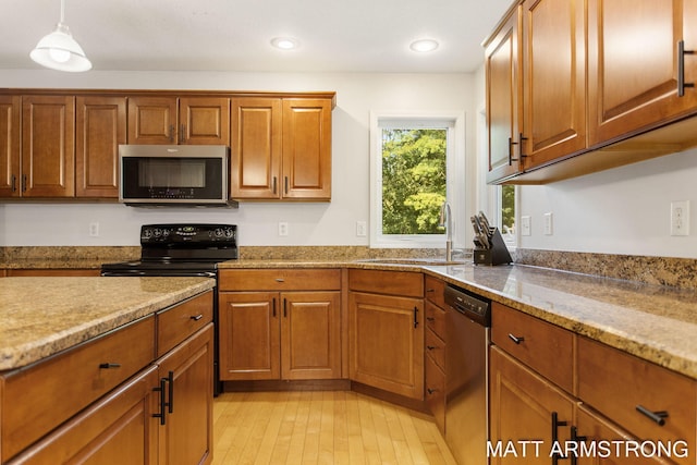 kitchen with pendant lighting, stainless steel appliances, light stone counters, sink, and light hardwood / wood-style floors