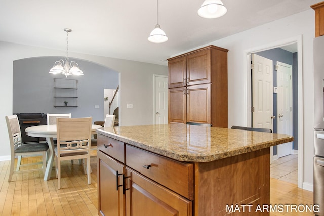 kitchen with light hardwood / wood-style flooring, pendant lighting, light stone counters, and a kitchen island