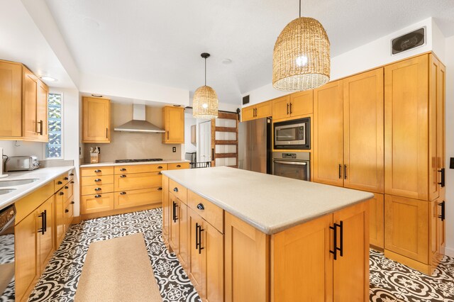 kitchen featuring appliances with stainless steel finishes, wall chimney exhaust hood, a kitchen island, and decorative light fixtures