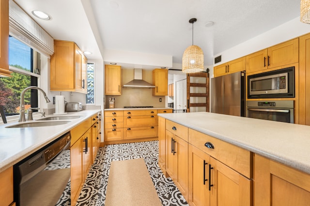 kitchen featuring sink, wall chimney range hood, stainless steel appliances, and decorative light fixtures