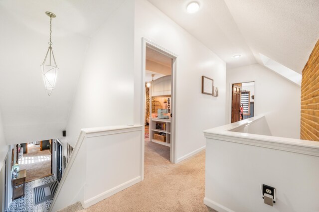 hallway with light carpet, lofted ceiling, and a textured ceiling