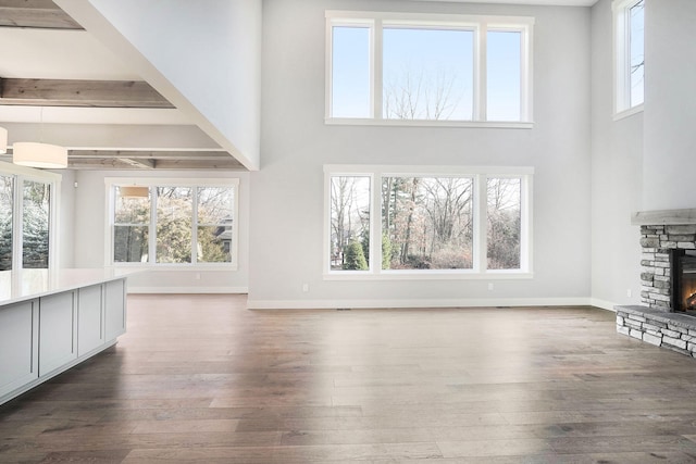 unfurnished living room with beam ceiling, a stone fireplace, dark wood-type flooring, and a towering ceiling