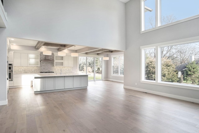 unfurnished living room with light hardwood / wood-style floors, a healthy amount of sunlight, and a high ceiling