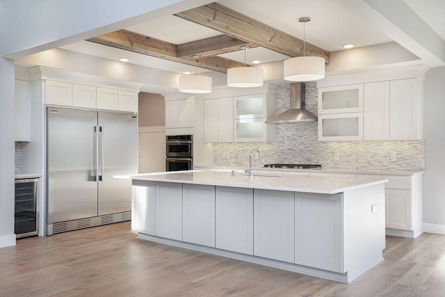 kitchen featuring pendant lighting, wall chimney range hood, appliances with stainless steel finishes, white cabinetry, and wine cooler