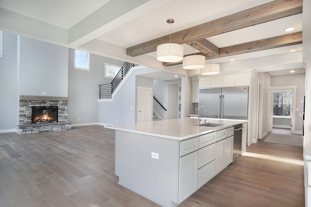 kitchen with beamed ceiling, sink, hanging light fixtures, a kitchen island with sink, and stainless steel appliances