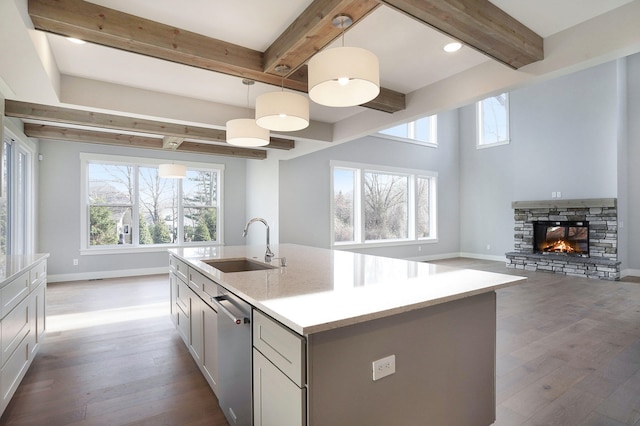 kitchen featuring a stone fireplace, pendant lighting, dishwasher, sink, and a center island with sink