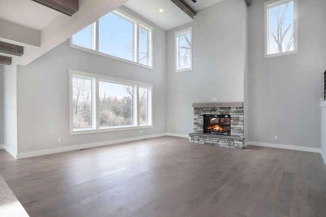 unfurnished living room with beam ceiling, wood-type flooring, a towering ceiling, and a fireplace