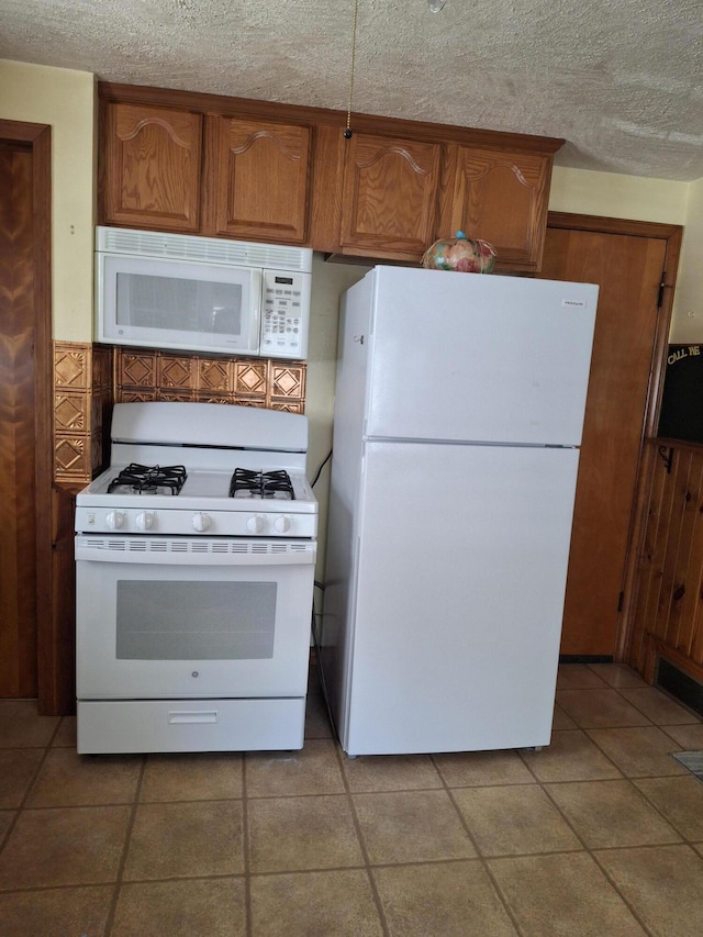 kitchen with a textured ceiling, light tile patterned floors, and white appliances