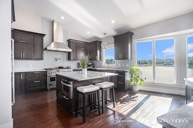 kitchen with tasteful backsplash, dark brown cabinetry, appliances with stainless steel finishes, wall chimney range hood, and vaulted ceiling