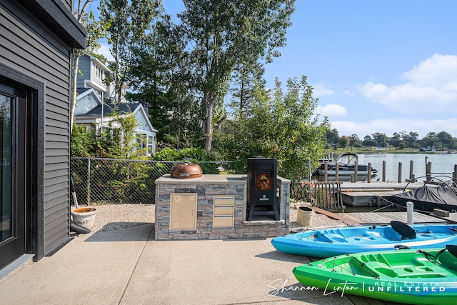 view of patio / terrace with a water view, exterior kitchen, a floating dock, and fence