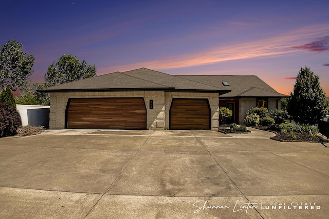 view of front facade with roof with shingles, a garage, brick siding, and concrete driveway