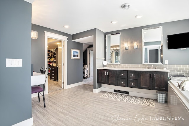 full bath featuring a sink, a tub, wood finished floors, a spacious closet, and double vanity