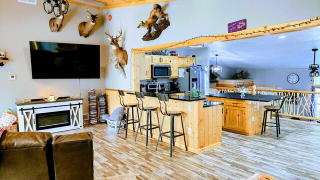 kitchen featuring a textured ceiling, stainless steel appliances, a center island, a breakfast bar area, and light hardwood / wood-style floors