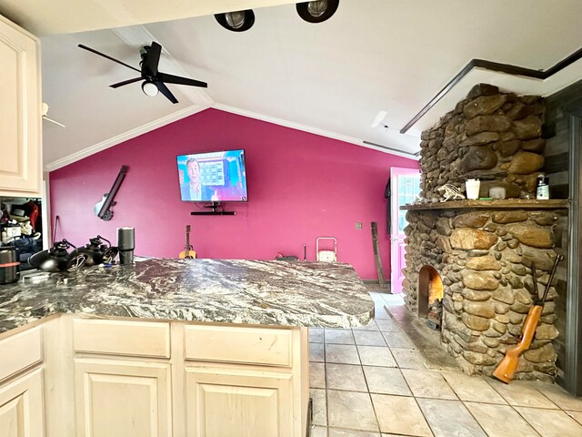 kitchen with a stone fireplace, light tile patterned floors, crown molding, lofted ceiling, and ceiling fan