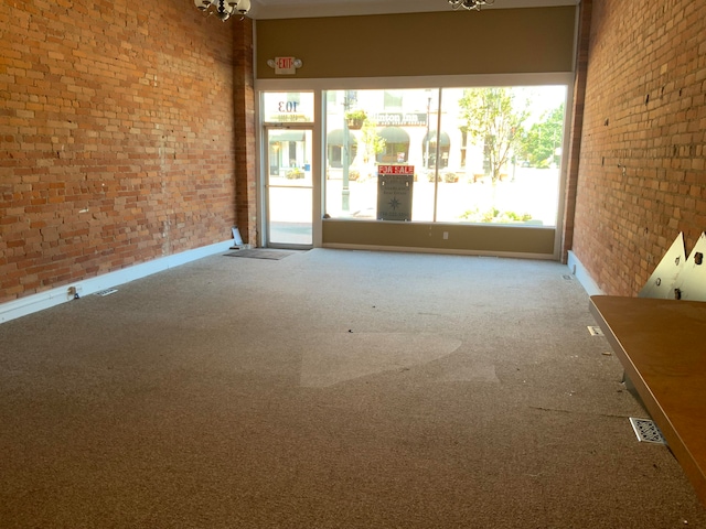 carpeted spare room featuring brick wall and a notable chandelier