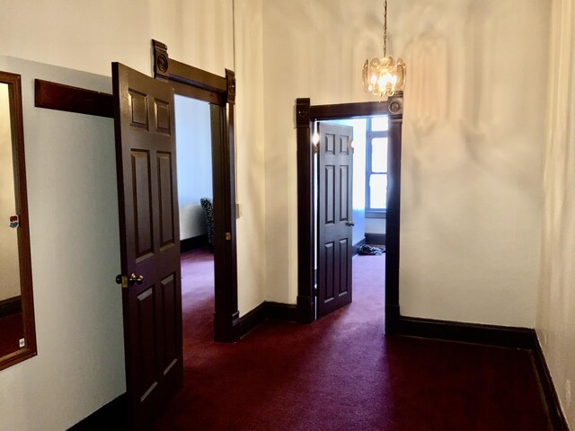 hall featuring an inviting chandelier and dark colored carpet