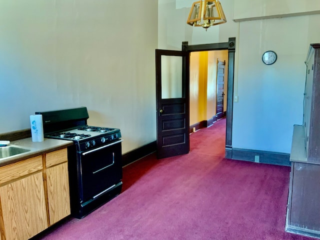 kitchen featuring dark colored carpet, light brown cabinetry, black gas stove, and hanging light fixtures