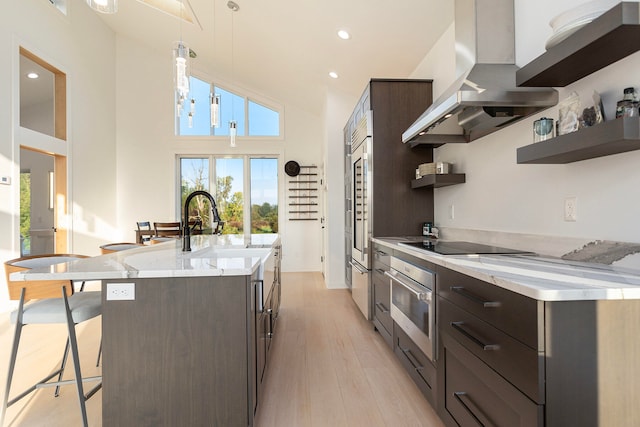 kitchen with a breakfast bar area, island range hood, hanging light fixtures, light hardwood / wood-style flooring, and oven