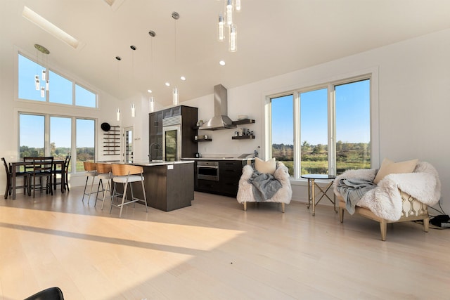 kitchen featuring wall chimney exhaust hood, pendant lighting, an island with sink, and a wealth of natural light